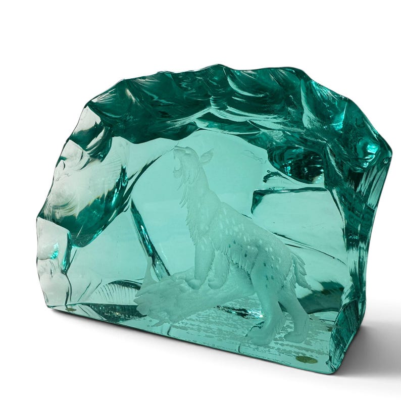 Peut inclure: Une sculpture en verre bleu sarcelle translucide repr&eacute;sentant un lynx sculpt&eacute; debout sur une b&ucirc;che. Le verre pr&eacute;sente un bord ext&eacute;rieur &eacute;pais, irr&eacute;gulier et textur&eacute; qui imite l'apparence d'une formation de glace naturelle, entourant la figurine.