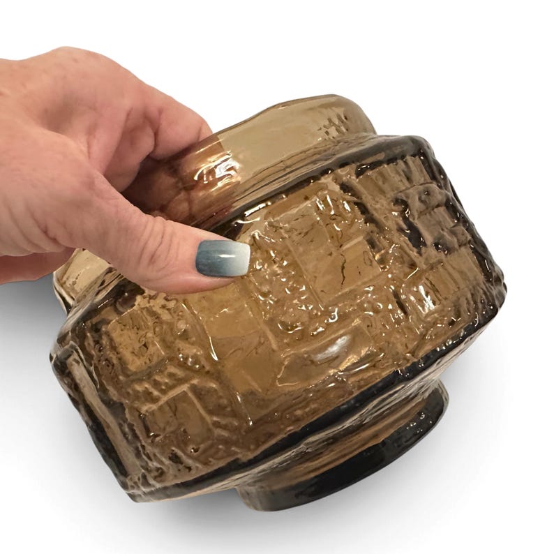 May include: A round, amber-colored glass bowl featuring a textured, raised geometric pattern on its exterior. The glass has a translucent quality with a smooth, wide rim and a slightly tapered base, showcasing a deep brown hue throughout.