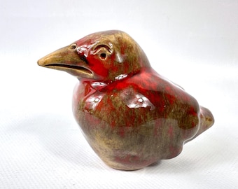 May include: A ceramic bird figurine with a glossy finish. The bird features a red and brown body with a yellow beak. The figurine is a decorative item, likely for display.