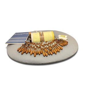 May include: A lace making kit featuring a round gray pillow, a yellow cylindrical bolster, numerous wooden bobbins with white thread, two spools of white thread, and a blue instructional book with the text Knyppling on the cover.