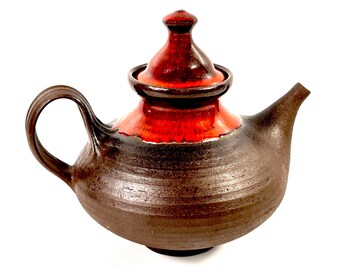 Puede incluir: Una tetera de cerámica artesanal con una base marrón oscuro y una sección superior y tapa rojas vibrantes. La tetera presenta un asa curva y un pico, perfecto para servir té. El diseño es simple y elegante, adecuado para cualquier cocina.