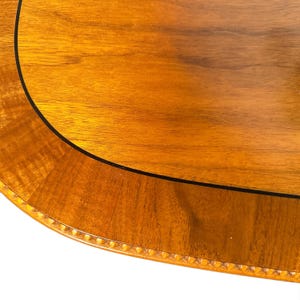 Op de afbeelding: Een gepolijst houten tafelblad met een warme bruine nerf, voorzien van een gebogen rand gedefinieerd door een dunne zwarte inleglijn en een decoratieve rand van kleine, gelijkmatig verdeelde uitgesneden kralen.