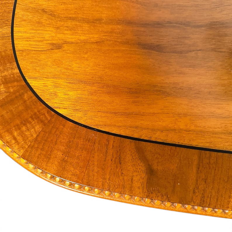 Op de afbeelding: Een gepolijst houten tafelblad met een warme bruine nerf, voorzien van een gebogen rand gedefinieerd door een dunne zwarte inleglijn en een decoratieve rand van kleine, gelijkmatig verdeelde uitgesneden kralen.