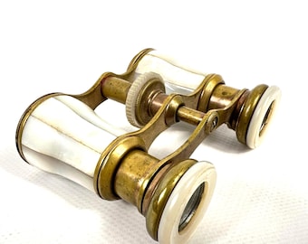 May include: Vintage opera glasses with a brass frame and white mother-of-pearl detailing. The antique binoculars feature a focus adjustment wheel and are designed for theatre viewing. The classic design is a beautiful collectible.