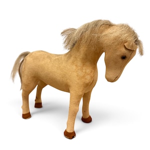 May include: A tan-colored plush horse figurine with a soft, felt-like texture. The horse features a light-colored synthetic mane and tail, dark brown hooves, and small, dark, round eyes. The head is positioned in a downward-facing posture.