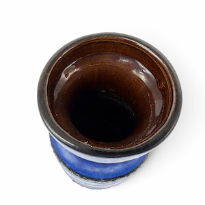 May include: A ceramic vase viewed from directly above, featuring a glossy dark brown interior glaze and a vibrant blue exterior finish. The rim is thick and dark, transitioning into a textured, mottled blue body that tapers slightly inward.