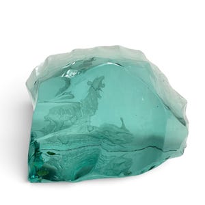 Peut inclure: Une sculpture en verre bleu sarcelle translucide en forme de roche dentel&eacute;e, pr&eacute;sentant un motif grav&eacute; d'un loup hurlant debout sur une surface rocheuse. Le verre poss&egrave;de des bords irr&eacute;guliers et facett&eacute;s ainsi qu'une surface avant lisse.