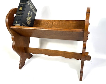 Könnte beinhalten: Ein Bücherregal aus Holz mit einem Regal und dekorativen Seitenteilen. Auf dem Regal liegt ein schwarzes Buch mit dem Titel "Necronomicon". Das Regal ist aus hellbraunem Holz gefertigt und hat ein robustes Design.