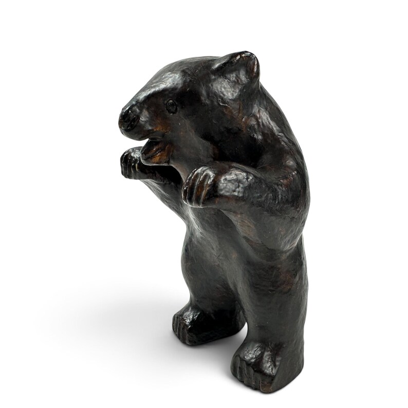 May include: A dark brown bear figurine standing on its hind legs with its front paws raised. The sculpture features a textured, glossy surface with visible carved details on the face, ears, and paws, capturing a dynamic, upright posture.