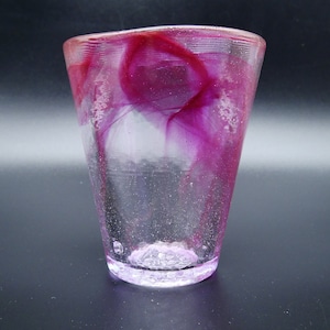 Puede incluir: Un vaso de vidrio transparente con forma acampanada, con dise&ntilde;os internos magenta y blancos arremolinados. La base y el borde tienen un aspecto texturizado. El vaso mide unos 10 cm de alto.