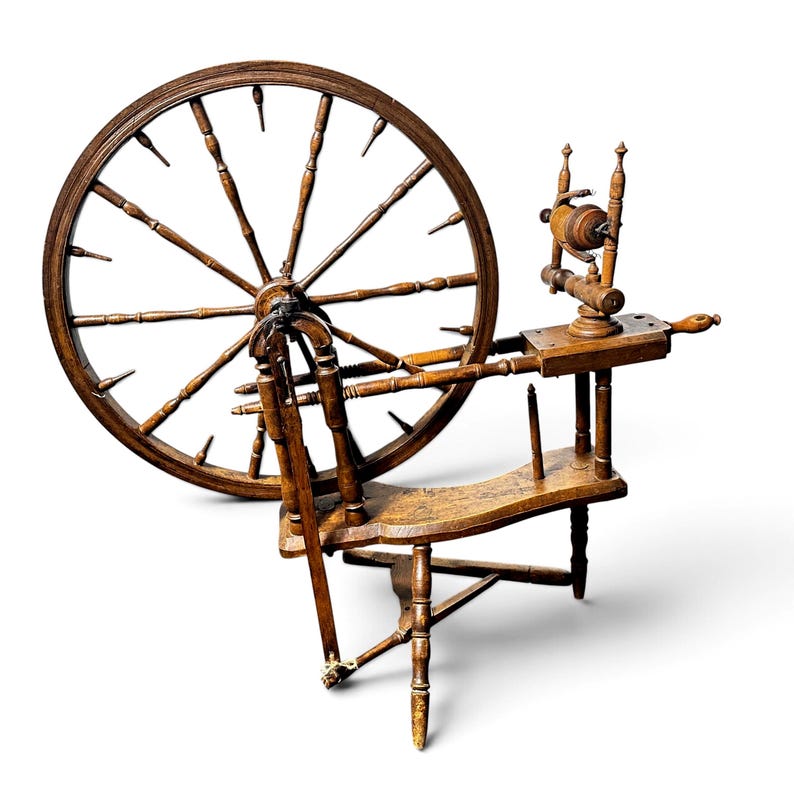 May include: A brown wooden spinning wheel featuring a large circular wheel with multiple spokes, a horizontal bench, a vertical flyer assembly with a bobbin, and a treadle mechanism supported by three legs, all constructed from dark stained wood.