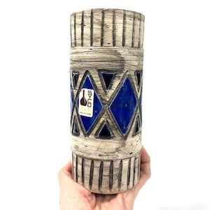 Peut inclure: Un vase en céramique blanche avec un motif géométrique bleu et blanc. Le vase a une surface texturée et une étiquette qui indique "SYCO Design for Garden".