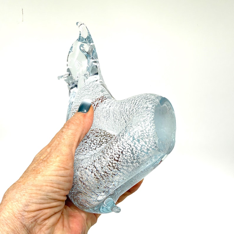 May include: A clear glass figurine shaped like a stylized cat, featuring a textured, frosted white interior pattern that creates a shimmering effect throughout the body, with a smooth, transparent glass head and pointed ears.