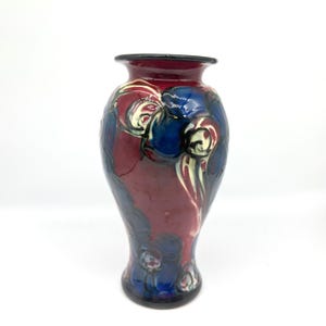 May include: A decorative ceramic vase with a dark red base and a black rim. The vase features a design of blue and white floral patterns. The vase is approximately 10 inches tall.