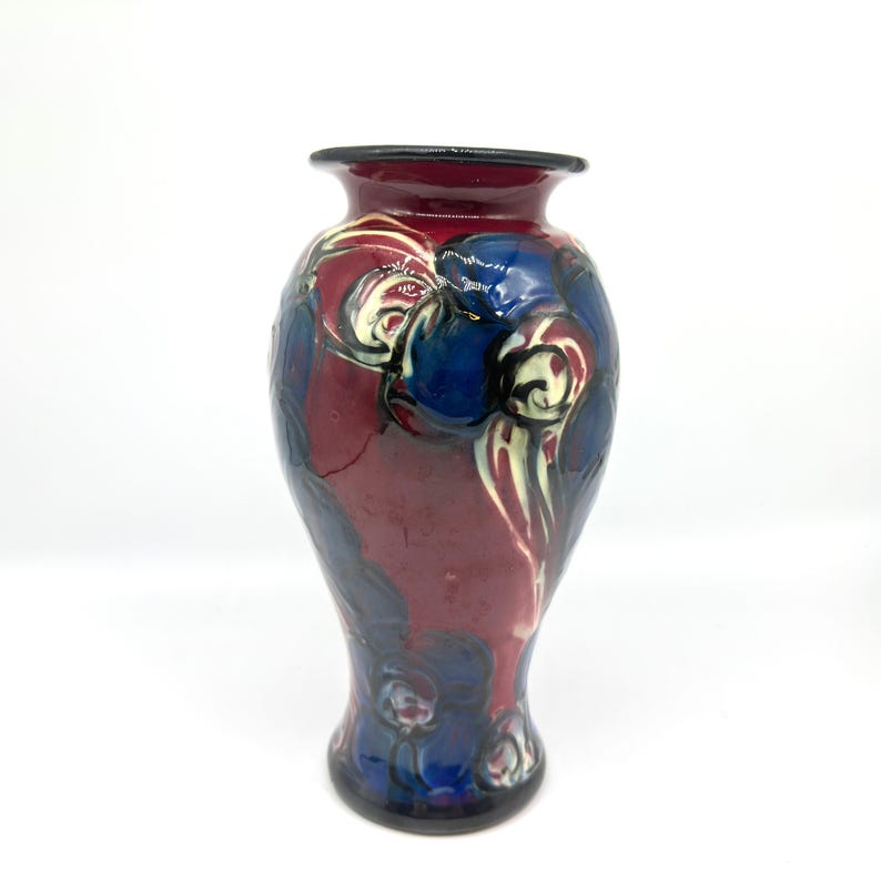 May include: A decorative ceramic vase with a dark red base and a black rim. The vase features a design of blue and white floral patterns. The vase is approximately 10 inches tall.