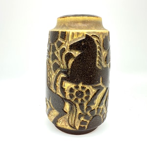 Peut inclure: Un vase cylindrique en c&eacute;ramique marron et beige. Le vase pr&eacute;sente un motif en relief de chevaux et de motifs floraux. Le bord sup&eacute;rieur est beige clair et la base est marron fonc&eacute;. Le vase a une surface textur&eacute;e. Hauteur d'environ 20 cm.