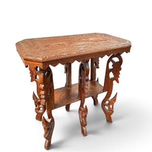 May include: A rectangular brown wooden side table featuring intricate hand-carved floral and leaf patterns on the tabletop and lower shelf. The table is supported by four ornate legs carved into stylized animal shapes with detailed textures.