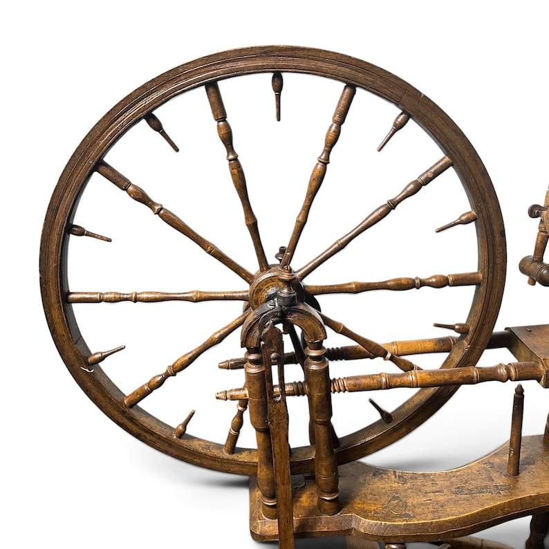 May include: A large, circular wooden spinning wheel with numerous thin, turned spokes radiating from a central hub. The structure is crafted from dark brown wood with a smooth, polished finish, featuring a horizontal base and vertical supports.