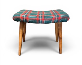 May include: A small, vintage stool with a plaid seat in shades of green, red, and blue. The seat is supported by four tapered wooden legs. The stool has a curved seat design and a classic, retro aesthetic.