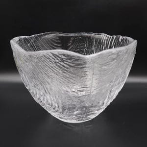 May include: A clear glass bowl featuring a textured, rippled surface that mimics the appearance of organic, flowing water. The bowl has an irregular, wavy rim and a deep, rounded basin, crafted from transparent glass with a reflective finish.