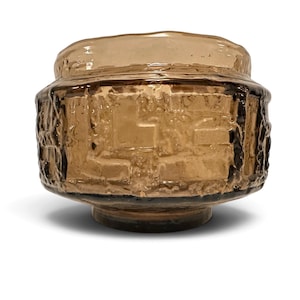 May include: A light brown glass bowl featuring a textured, relief-patterned exterior with a wide, rounded body and a smooth, circular rim. The glass has a translucent quality with varying depths of color and a thick, heavy appearance.