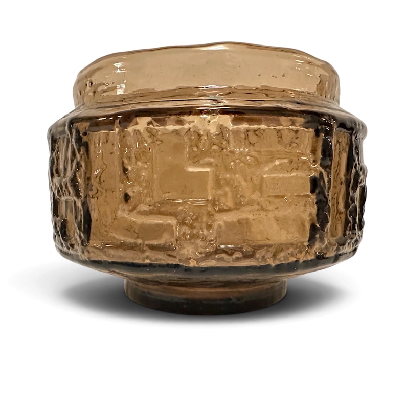 May include: A light brown glass bowl featuring a textured, relief-patterned exterior with a wide, rounded body and a smooth, circular rim. The glass has a translucent quality with varying depths of color and a thick, heavy appearance.