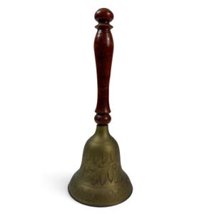 May include: A hand bell featuring a polished brass body with an etched floral pattern and a smooth, dark brown wooden handle. The bell has a flared base and a rounded top knob on the handle, providing a clear contrast between the metal and wood.