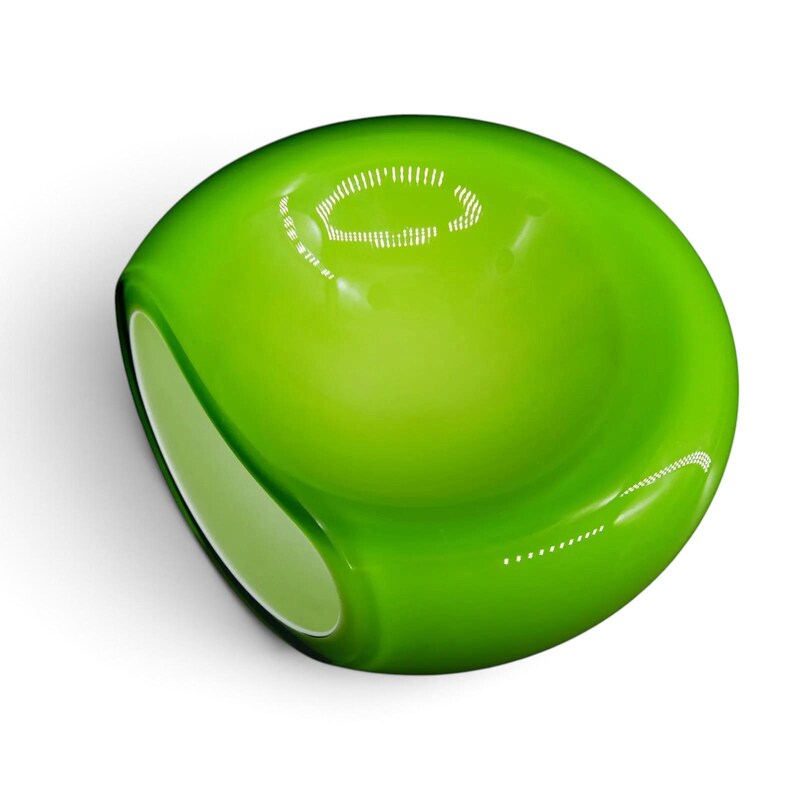 May include: A smooth, rounded glass object in a vibrant lime green color. The piece features a polished, reflective surface with a concave center and a flattened side, showcasing a translucent quality that catches light with bright white highlights.