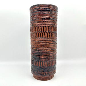 Può includere: Un vaso cilindrico alto in ceramica con un designo testurizzato marrone e nero. Il vaso ha un'ampia apertura e una base stretta.