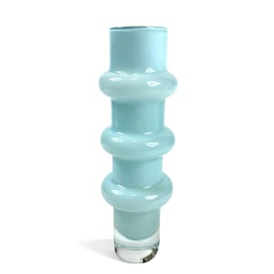 May include: A tall, cylindrical glass vase in a pale, translucent light blue color. The vase features three distinct, rounded horizontal ridges or rings stacked vertically along its body, with a smooth, clear glass base at the bottom.