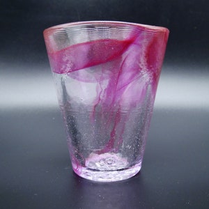Puede incluir: Un vaso de vidrio transparente con forma acampanada y superficie texturizada. El vidrio presenta un dise&ntilde;o vibrante y arremolinado de tonos magenta y rosa en el interior, creando un efecto visual &uacute;nico. La base es de un tono rosa m&aacute;s claro.