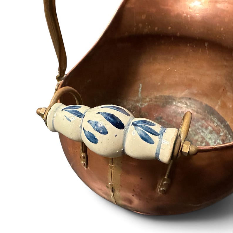 Pu&ograve; includere: Un secchio per carbone in rame con finitura metallica lucida e manico curvo. L'impugnatura &egrave; caratterizzata da una presa in ceramica bianca decorata con motivi a foglie blu dipinti a mano, fissata con componenti in metallo color ottone.