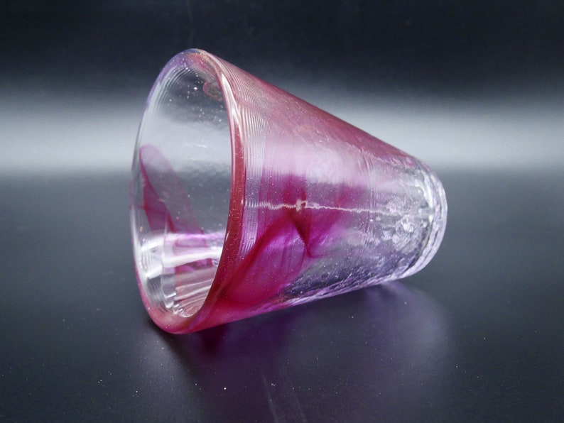 Puede incluir: Un vaso de vidrio transparente con un interior y borde magenta vibrante. El vidrio tiene una apariencia texturizada, ligeramente esmerilada, con estr&iacute;as verticales en la parte inferior. El color magenta se arremolina y se mezcla dentro del vidrio.