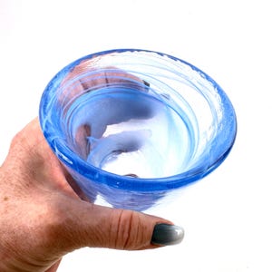 Puede incluir: Un cuenco de vidrio soplado a mano con un vibrante dise&ntilde;o de remolino azul y blanco. El cuenco tiene una forma redondeada con una amplia abertura y un borde grueso y resistente. El vidrio transl&uacute;cido permite el paso de la luz, creando un hermoso efecto.