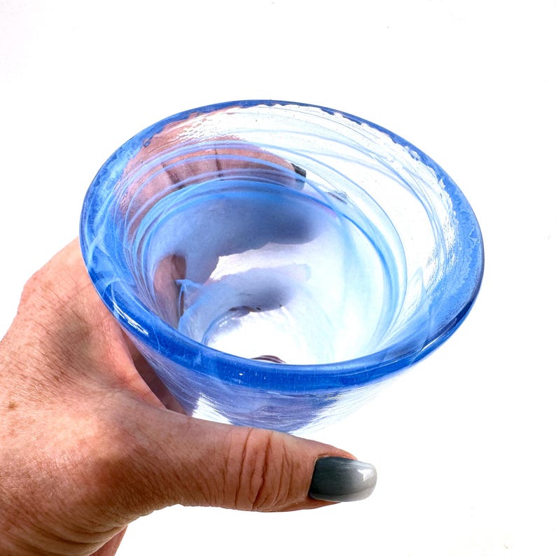 Puede incluir: Un cuenco de vidrio soplado a mano con un vibrante dise&ntilde;o de remolino azul y blanco. El cuenco tiene una forma redondeada con una amplia abertura y un borde grueso y resistente. El vidrio transl&uacute;cido permite el paso de la luz, creando un hermoso efecto.