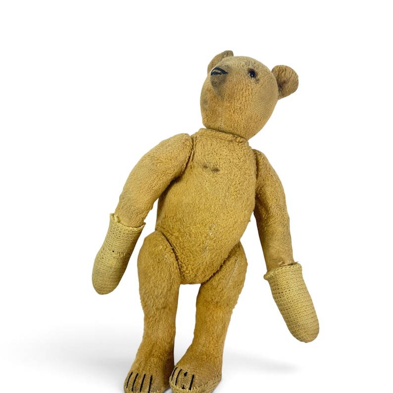 Pode incluir: Um urso de peluche castanho de estilo vintage com pelo gasto, apresentando olhos escuros costurados e um nariz escuro. O urso tem punhos de malha de cor clara nos bra&ccedil;os e detalhes de garras costurados nos p&eacute;s, em posi&ccedil;&atilde;o vertical.