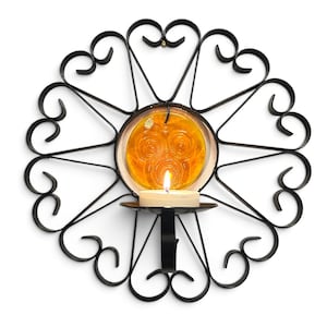 Peut inclure: Une applique murale en m&eacute;tal noir dot&eacute;e d'un cadre circulaire avec des volutes d&eacute;coratives et des accents en forme de c&oelig;ur. Un insert en verre ambr&eacute; translucide est plac&eacute; au centre, avec une petite bougie chauffe-plat blanche allum&eacute;e.