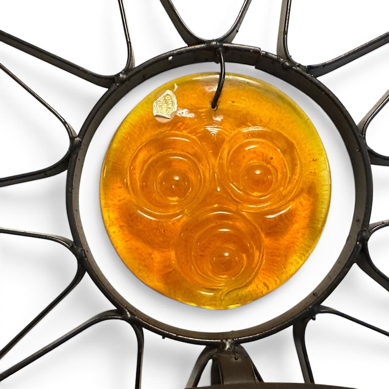 Peut inclure: Une d&eacute;coration murale en forme de soleil compos&eacute;e d'un &eacute;l&eacute;ment central en verre ambr&eacute; circulaire orn&eacute; de trois motifs en spirale en relief. Le verre est ench&acirc;ss&eacute; dans un cadre en m&eacute;tal sombre avec des rayons qui s'&eacute;tendent vers l'ext&eacute;rieur.