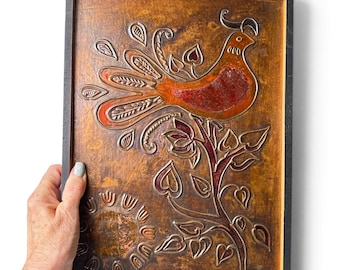 May include: A rectangular wall plaque featuring a copper-toned embossed design of a bird perched on a leafy branch with a sun motif below. The artwork is set within a dark wooden frame and includes the signature FALE inscribed at the bottom.