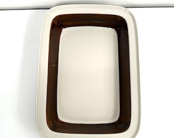 May include: A rectangular ceramic baking dish featuring a smooth cream-colored center basin surrounded by a wide, dark brown glazed border. The outer rim is finished with a subtle, embossed geometric pattern in a matching cream color.