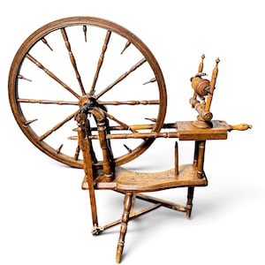 May include: A brown wooden spinning wheel featuring a large circular wheel with numerous spokes, a horizontal bench, a vertical flyer assembly with a bobbin, and a tripod base. The structure is crafted from turned wood components throughout.