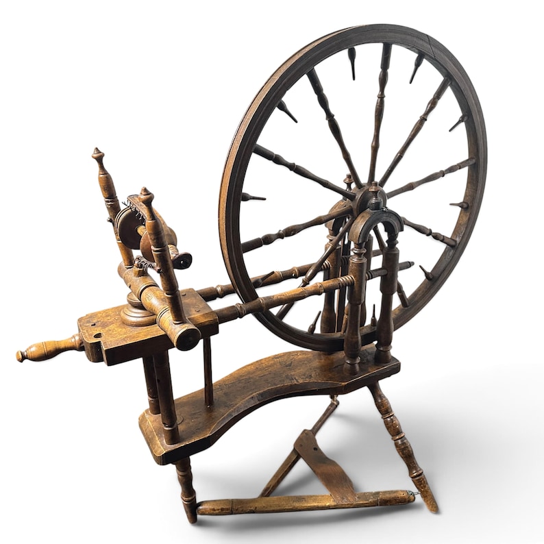 May include: A brown wooden spinning wheel featuring a large circular wheel with multiple spokes, a horizontal frame, a treadle mechanism at the base, and a flyer assembly with a bobbin, all constructed from dark stained wood with turned details.