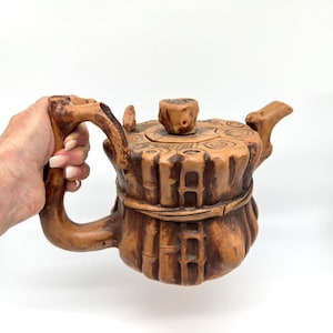 以下が含まれることがあります： 蓋と取っ手が付いた茶色のセラミックティーポット。 ティーポットは、竹のようなディテールと蓋の円形模様を備えたテクスチャード加工された表面を持っています。 ハンドルと注ぎ口は素朴で有機的なデザインです。