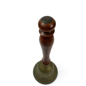 May include: A hand bell featuring a dark brown wooden handle with a rounded top knob and a flared brass base. The brass bell section displays a subtle, engraved floral pattern around its circumference, showing a weathered, aged metal finish.