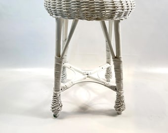 May include: A white wicker stool featuring a round woven seat and four legs connected by a central X-shaped support brace. The structure is crafted from coiled white rattan material with reinforced wrapped joints at the base of each leg.