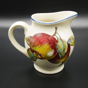 May include: A white ceramic jug with a blue rim and a painted design of red apples with green leaves.
