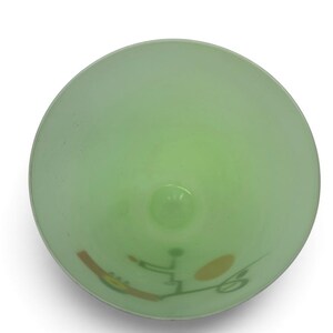 K&ouml;nnte beinhalten: Eine hellgr&uuml;ne Glasschale, direkt von oben betrachtet. Die Innenfl&auml;che zeigt ein grafisches Design, das aus einer braunen rechteckigen Form, einem gelben Oval und d&uuml;nnen dunkelgr&uuml;nen Linien besteht, die abstrakte Muster bilden.