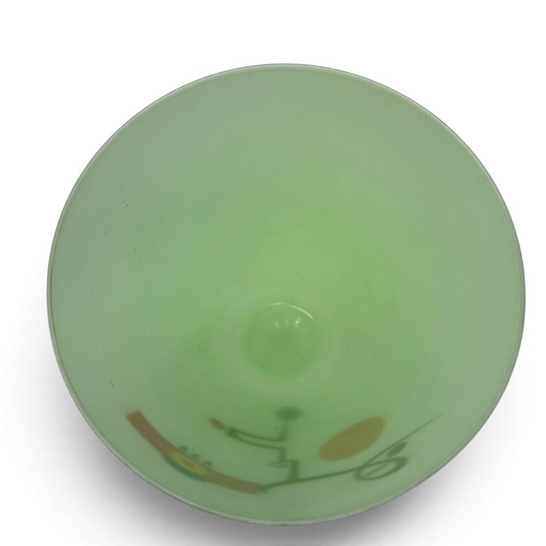 K&ouml;nnte beinhalten: Eine hellgr&uuml;ne Glasschale, direkt von oben betrachtet. Die Innenfl&auml;che zeigt ein grafisches Design, das aus einer braunen rechteckigen Form, einem gelben Oval und d&uuml;nnen dunkelgr&uuml;nen Linien besteht, die abstrakte Muster bilden.