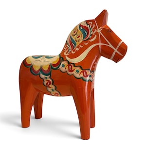 Puede incluir: Una figura de caballo de madera tallada pintada en un tono naranja vibrante. El caballo presenta intrincados patrones florales y geom&eacute;tricos pintados a mano en tonos azul, amarillo, verde y blanco en la crin, el lomo y los costados.