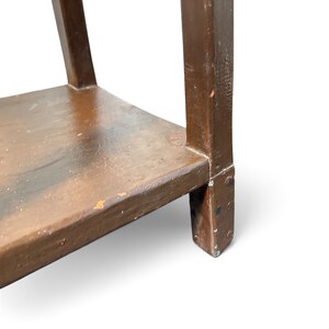 May include: A brown wooden side table with a rectangular shelf and four straight legs. The surface of the wood shows signs of wear with visible paint chips and a textured finish. The structure is composed of solid wood components joined together.